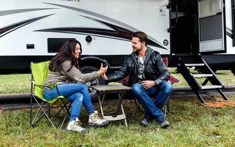 a man and a woman are sitting in front of a trailer that says rv on it