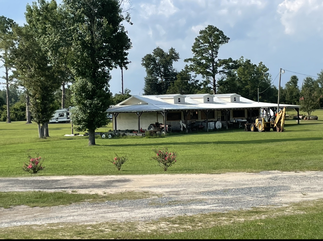 A large white house is sitting in the middle of a grassy field.