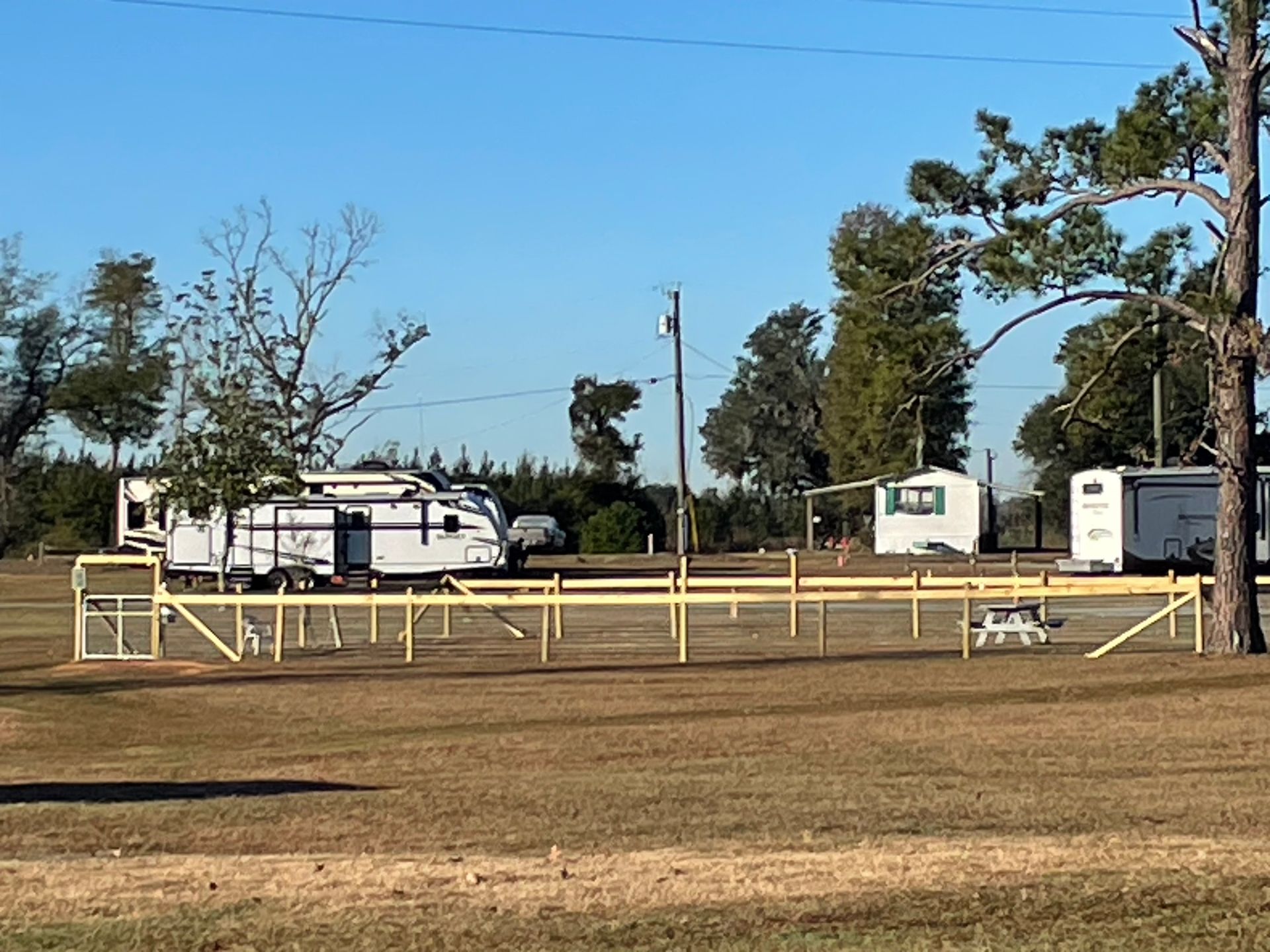 A rv is parked in a field next to a wooden fence.