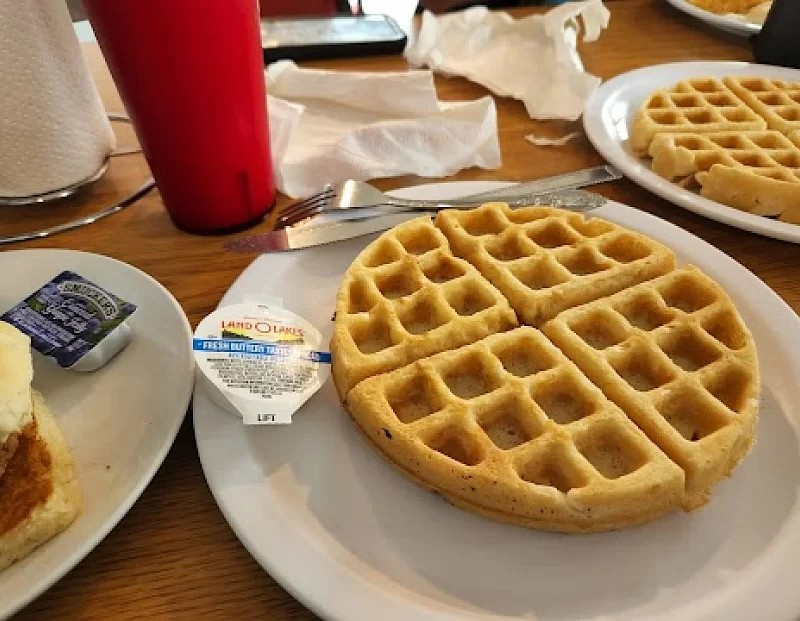 A waffle on a white plate with butter on it