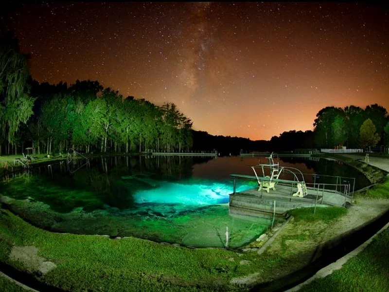 A swimming pool is lit up at night with a starry sky in the background.