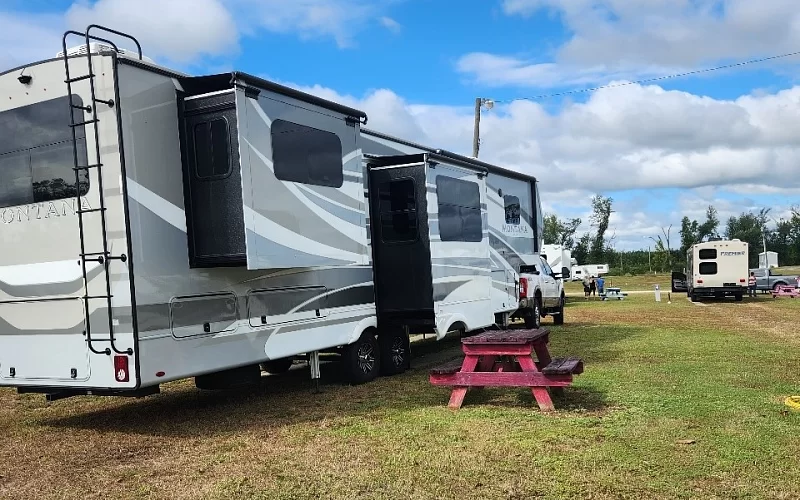 A rv is parked in a grassy field next to a picnic table.