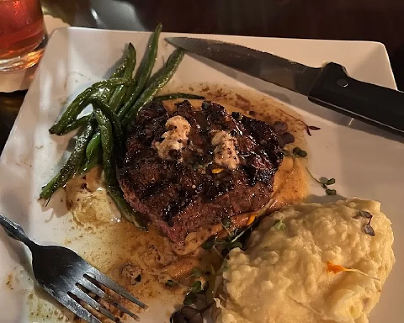 A white plate topped with a steak green beans and mashed potatoes.