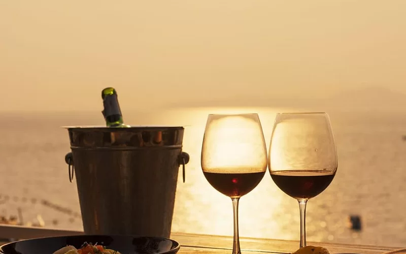 two glasses of wine and a bucket of wine are on a table in front of the ocean .