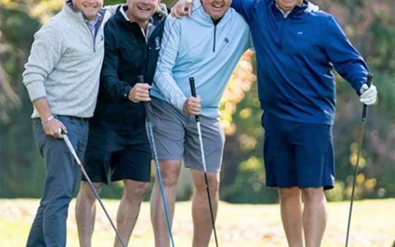 A group of men are standing next to each other on a golf course holding golf clubs.
