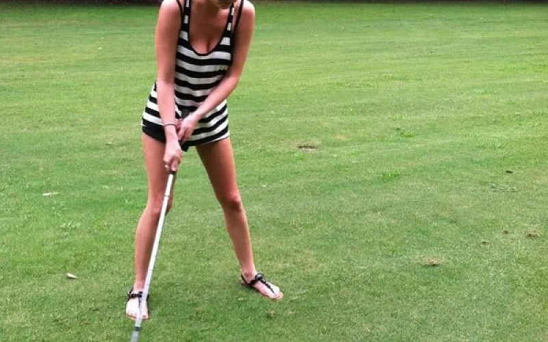 A woman is swinging a golf club on a golf course.