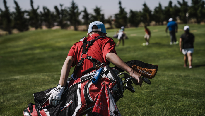 A view of a golfer in a red top carrying his club bag