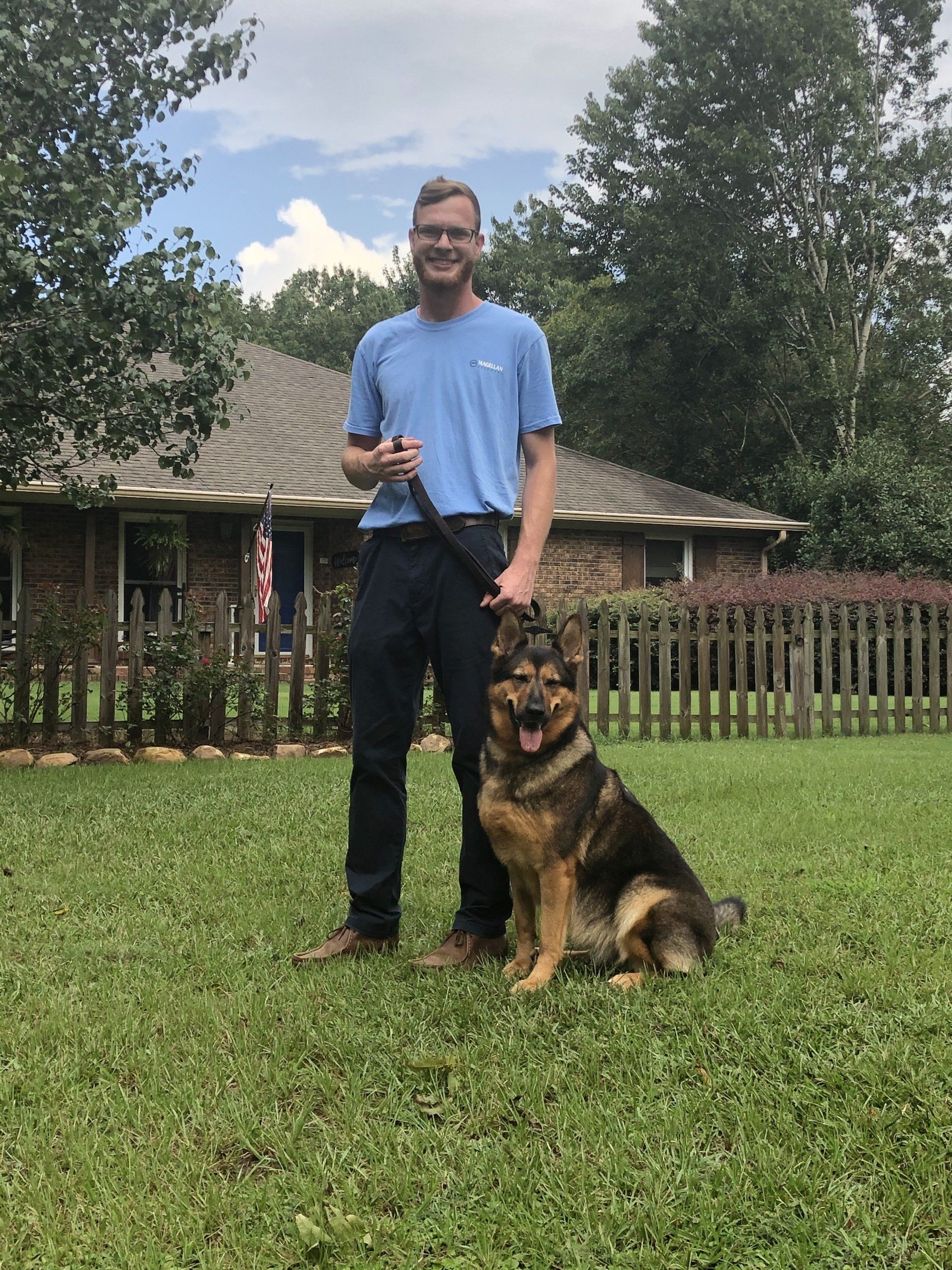A man is standing next to a german shepherd in a yard.
