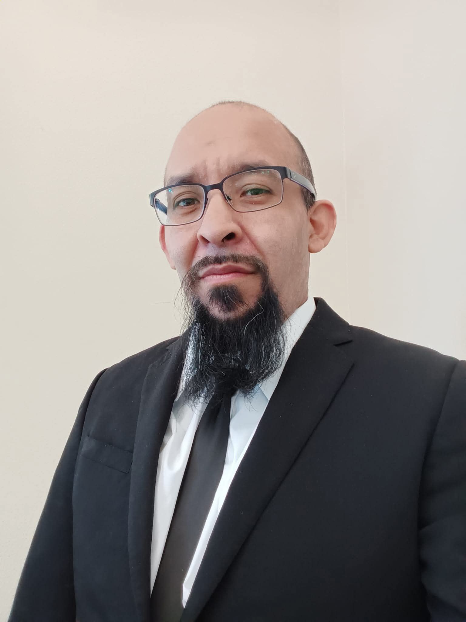 A man with a beard and glasses is wearing a suit and tie.