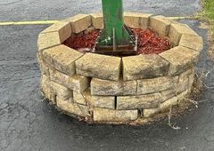 A green pole is sitting in a stone planter on the side of the road.