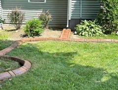 A lush green lawn with a brick walkway in front of a house.