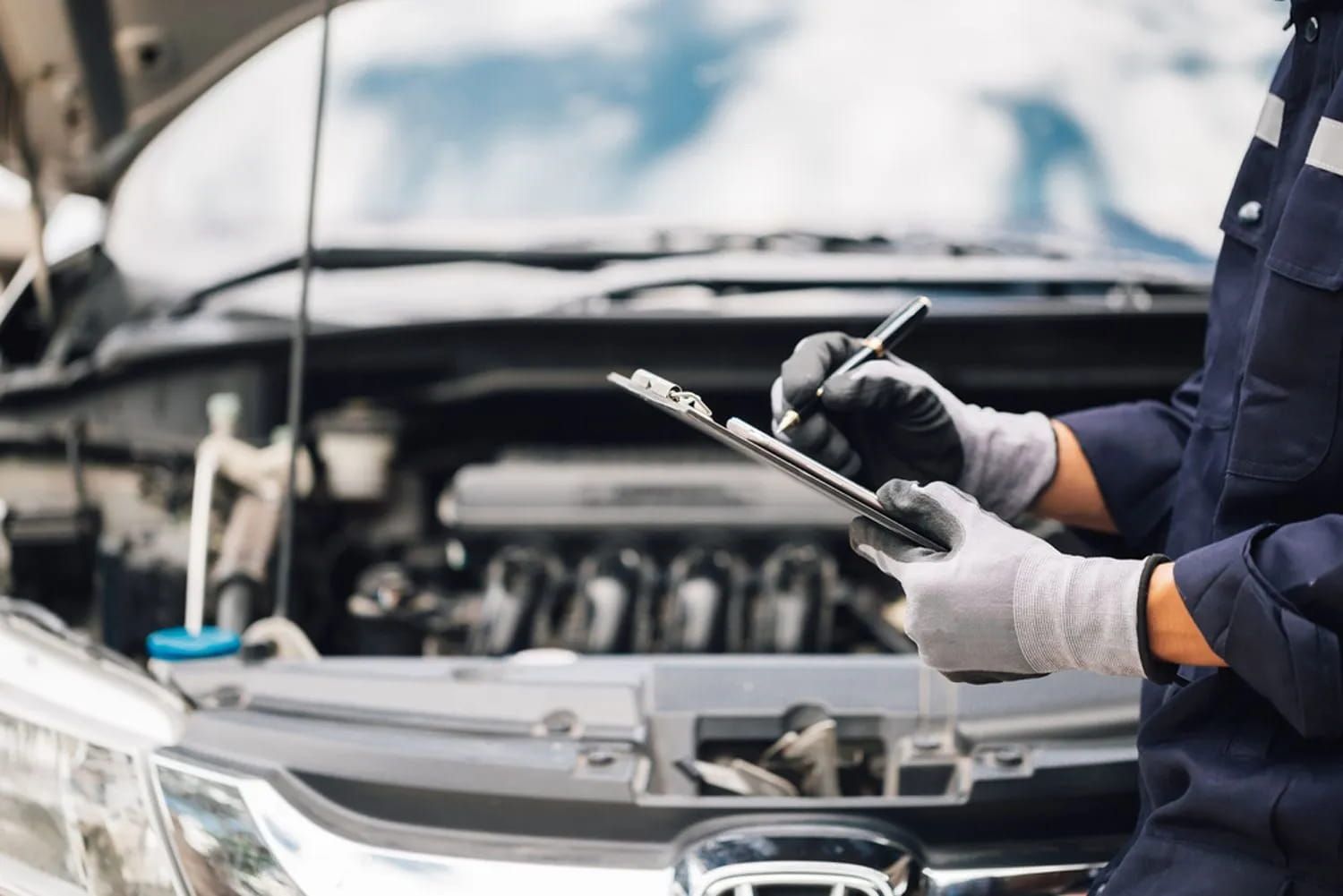 A Mechanic is Writing on a Clipboard in Front of a Car — Fosters Ace Auto Repairs In Aitkenvale, QLD