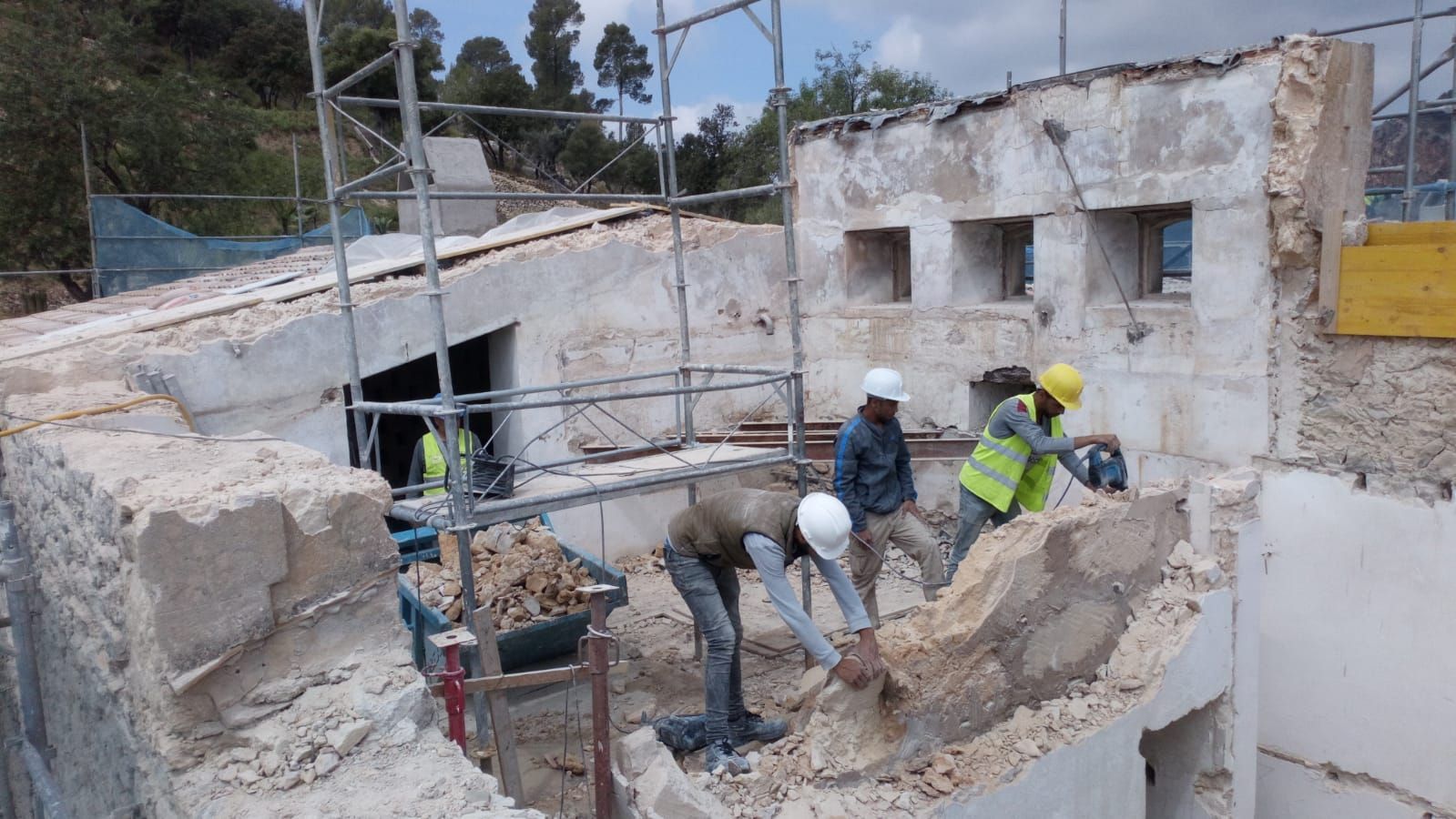 Obreros  CAN RAMIS obras y reformas demoliendo un edificio con andamios, equipados con cascos y chalecos de seguridad.