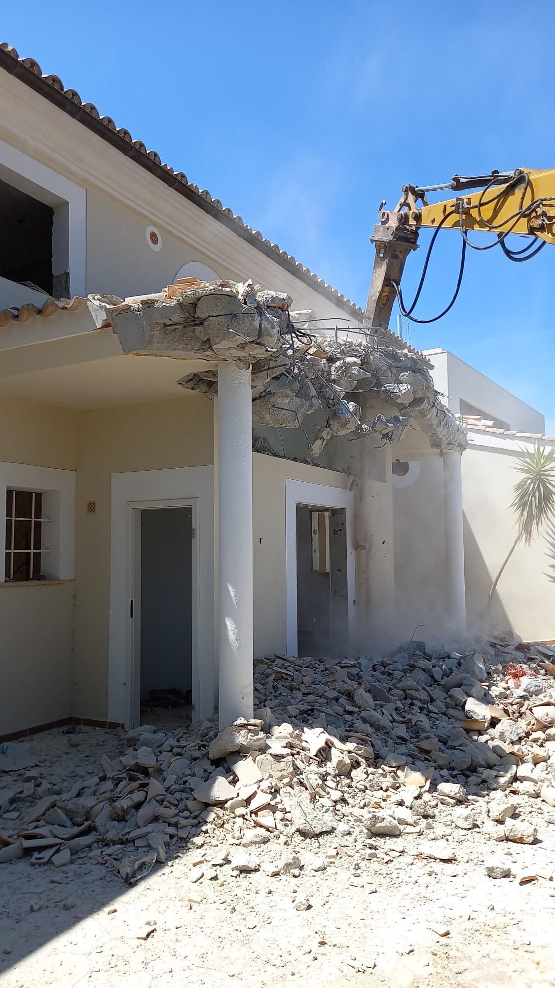 Demolición de la fachada de un edificio con una excavadora a cielo abierto. Montones de escombros abajo.