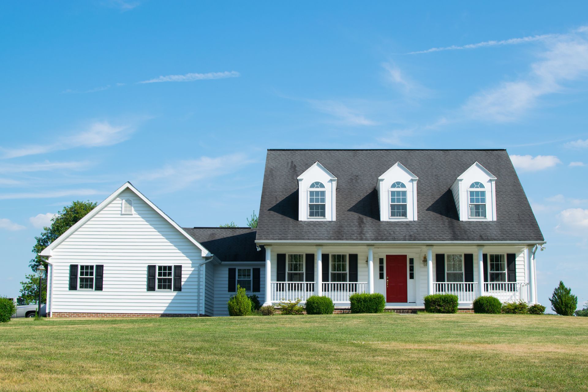 White two-story house with black roof, red door, and green lawn under a blue sky.