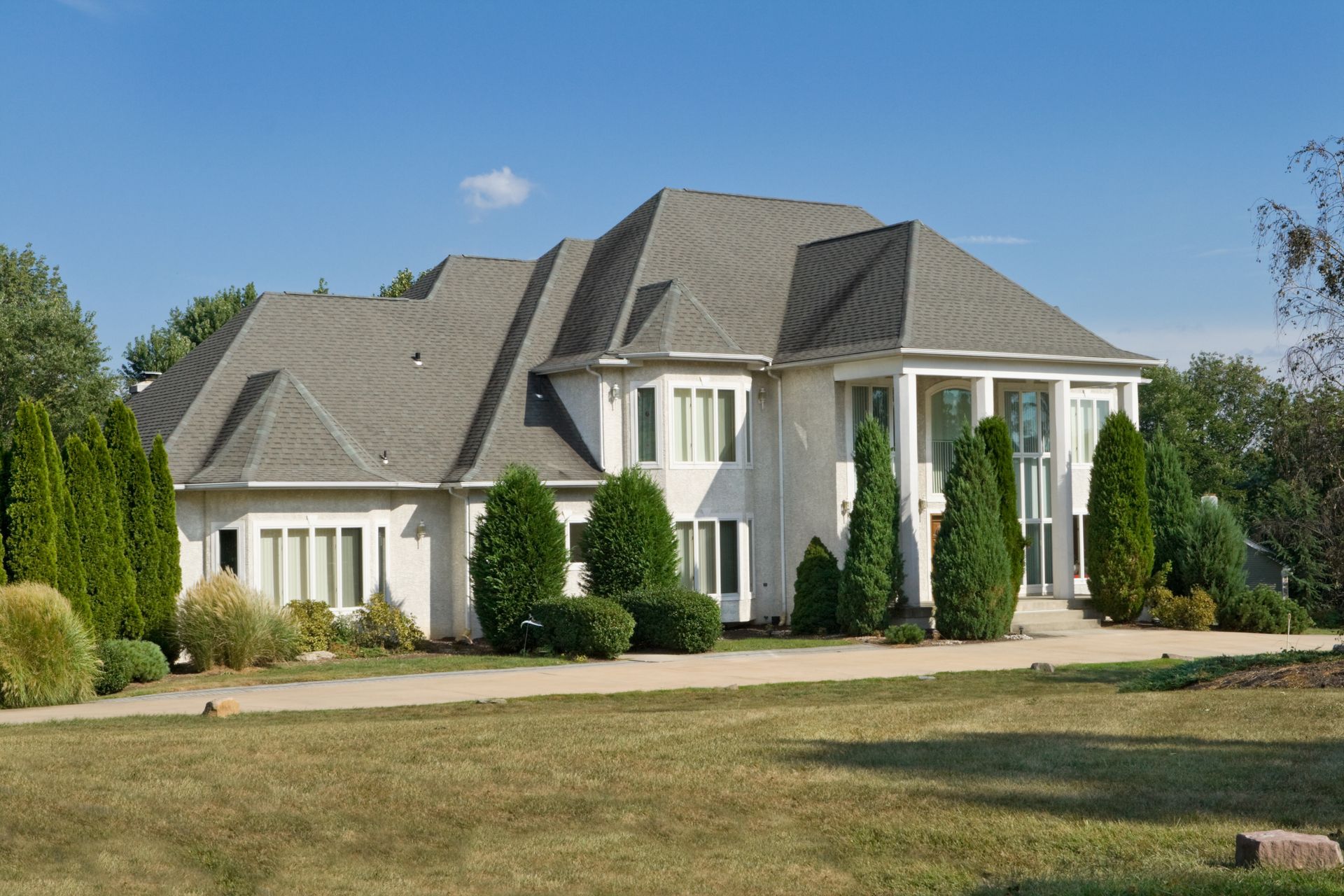 White house with a gray roof, lawn, and trees under a blue sky.