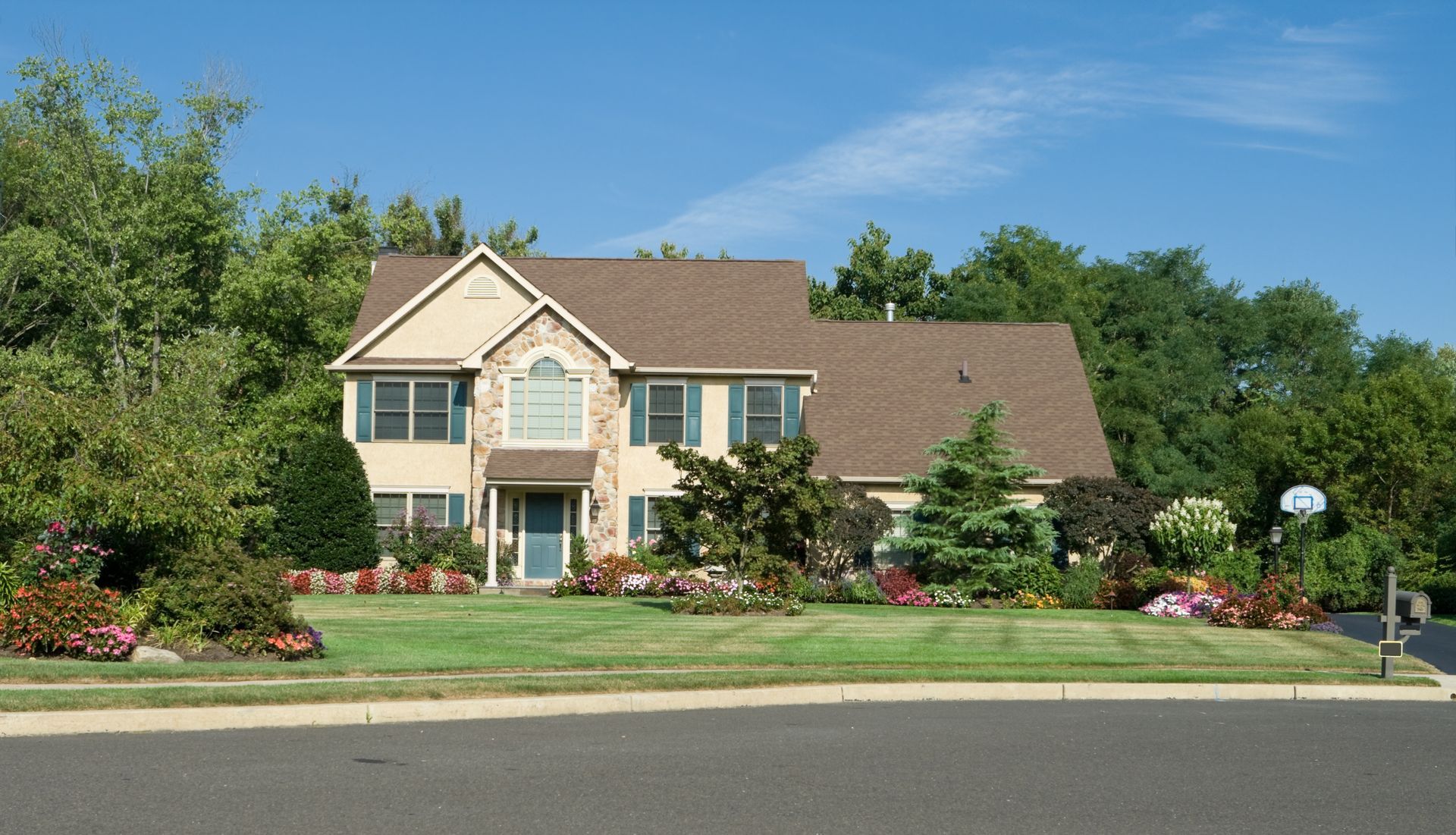 Two-story beige house with a brown roof and a well-manicured lawn on a sunny day.