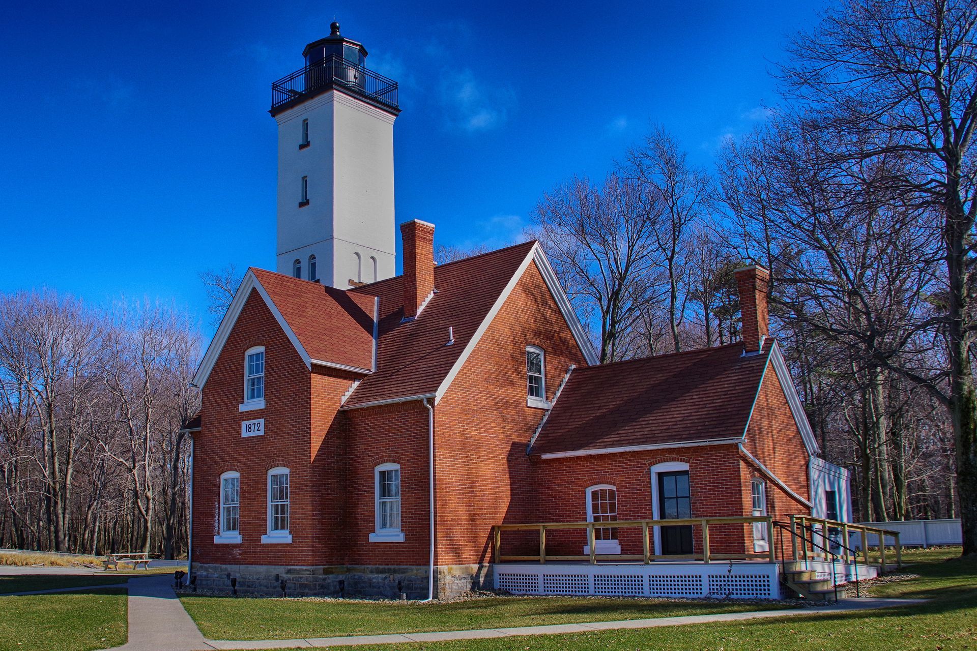 Brick lighthouse with a tall white tower, against a clear blue sky.