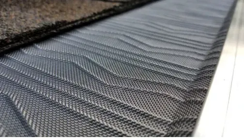 Leaves in a gutter with a mesh guard, brown and green grass in background.