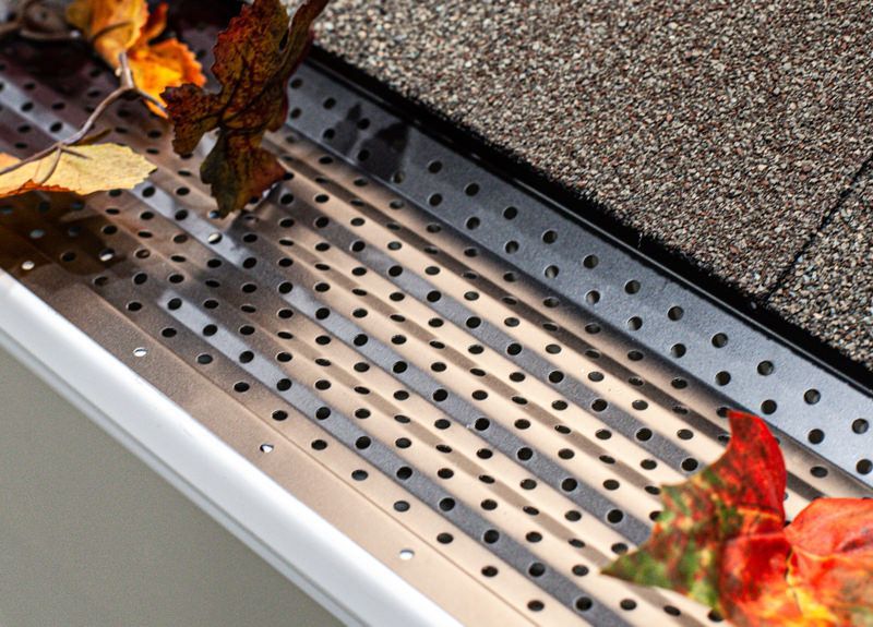 Gutter with black mesh guard installed near roof shingles to prevent debris accumulation.