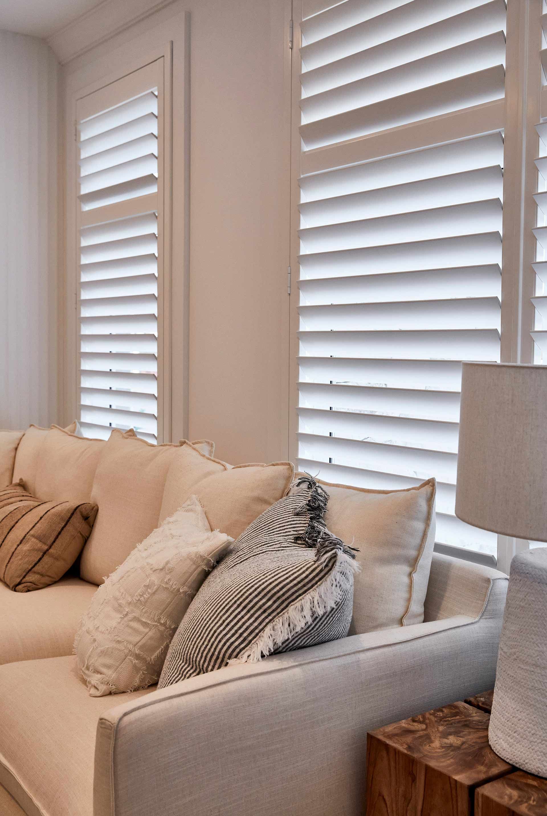 A living room with a couch , lamp , and shutters on the windows.