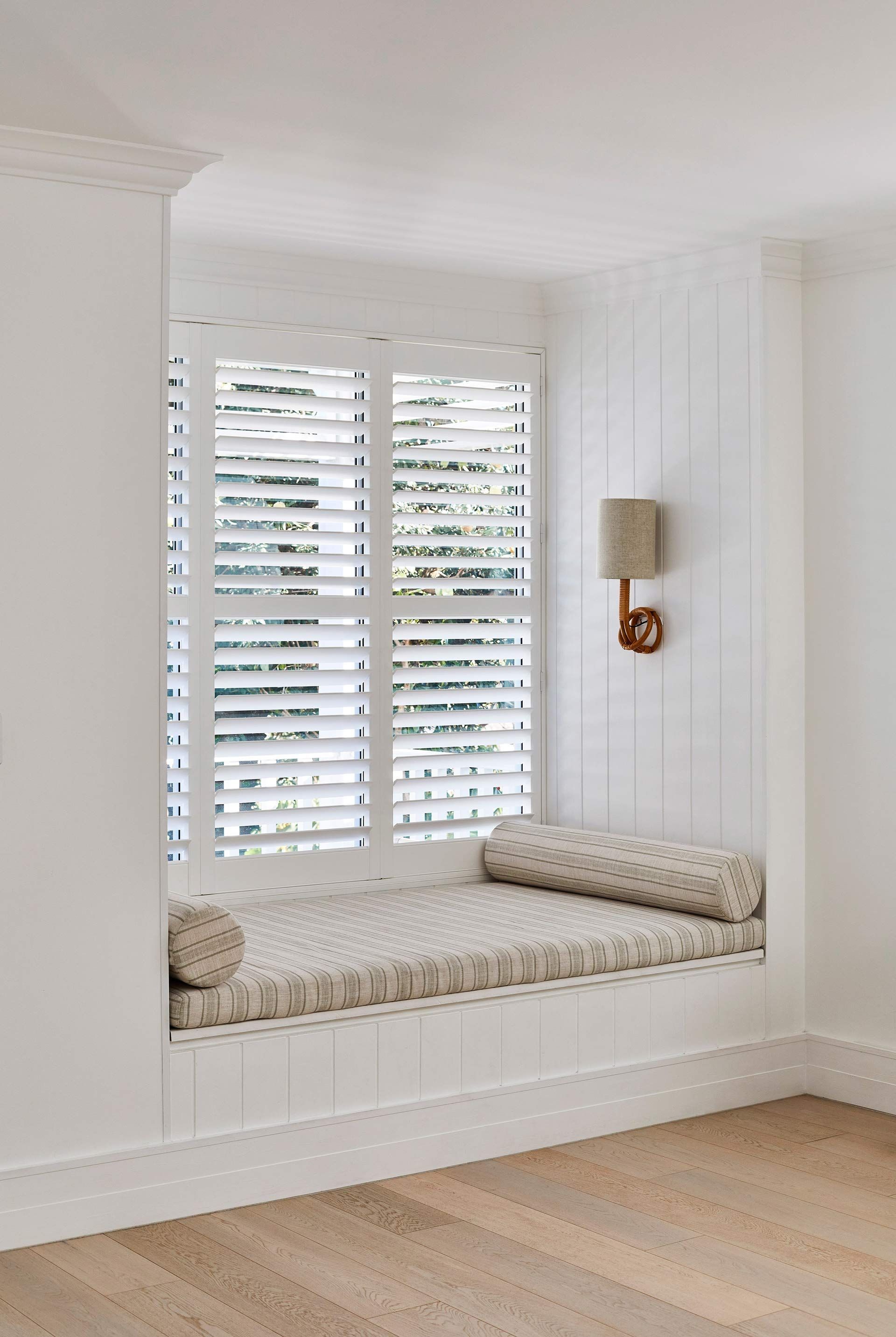 A window seat with shutters and a lamp in a room.