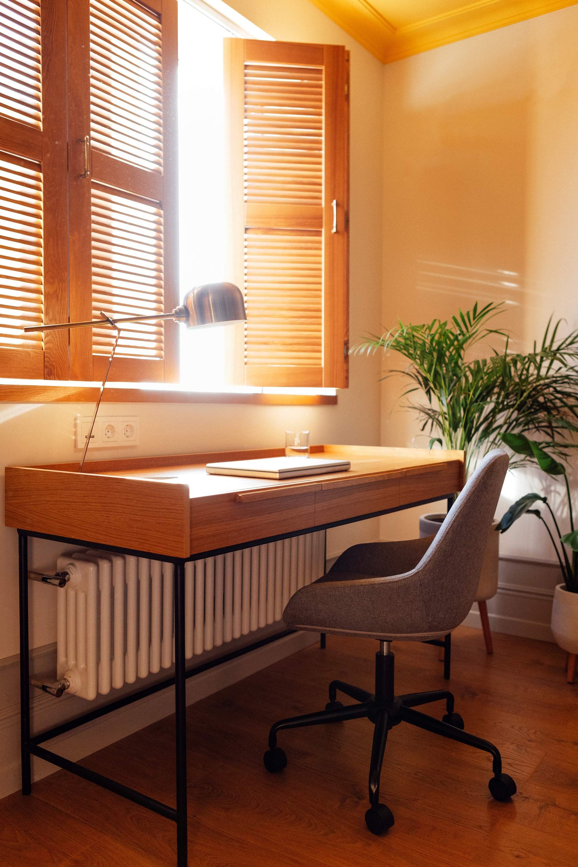 A wooden desk with a chair in front of a window.