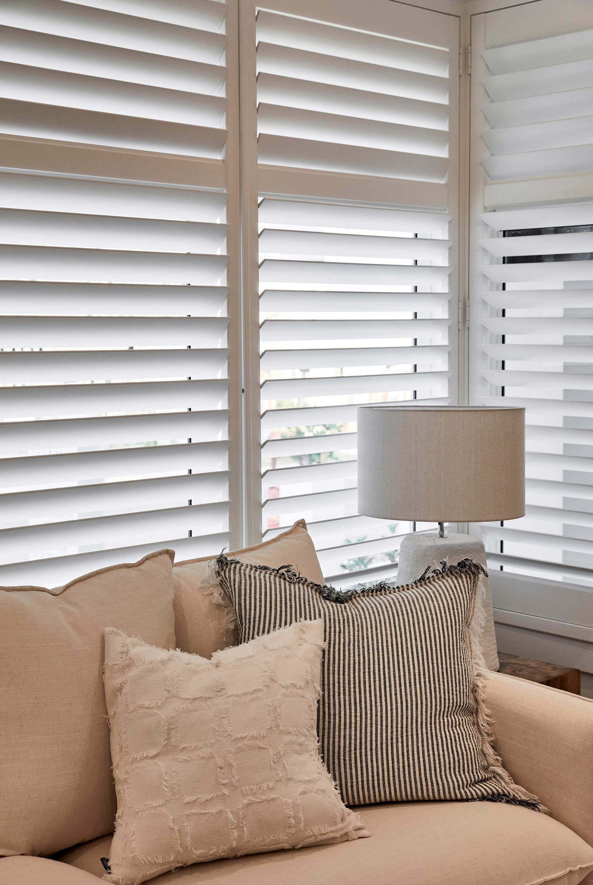 A living room with a couch , lamp , and shutters on the windows.