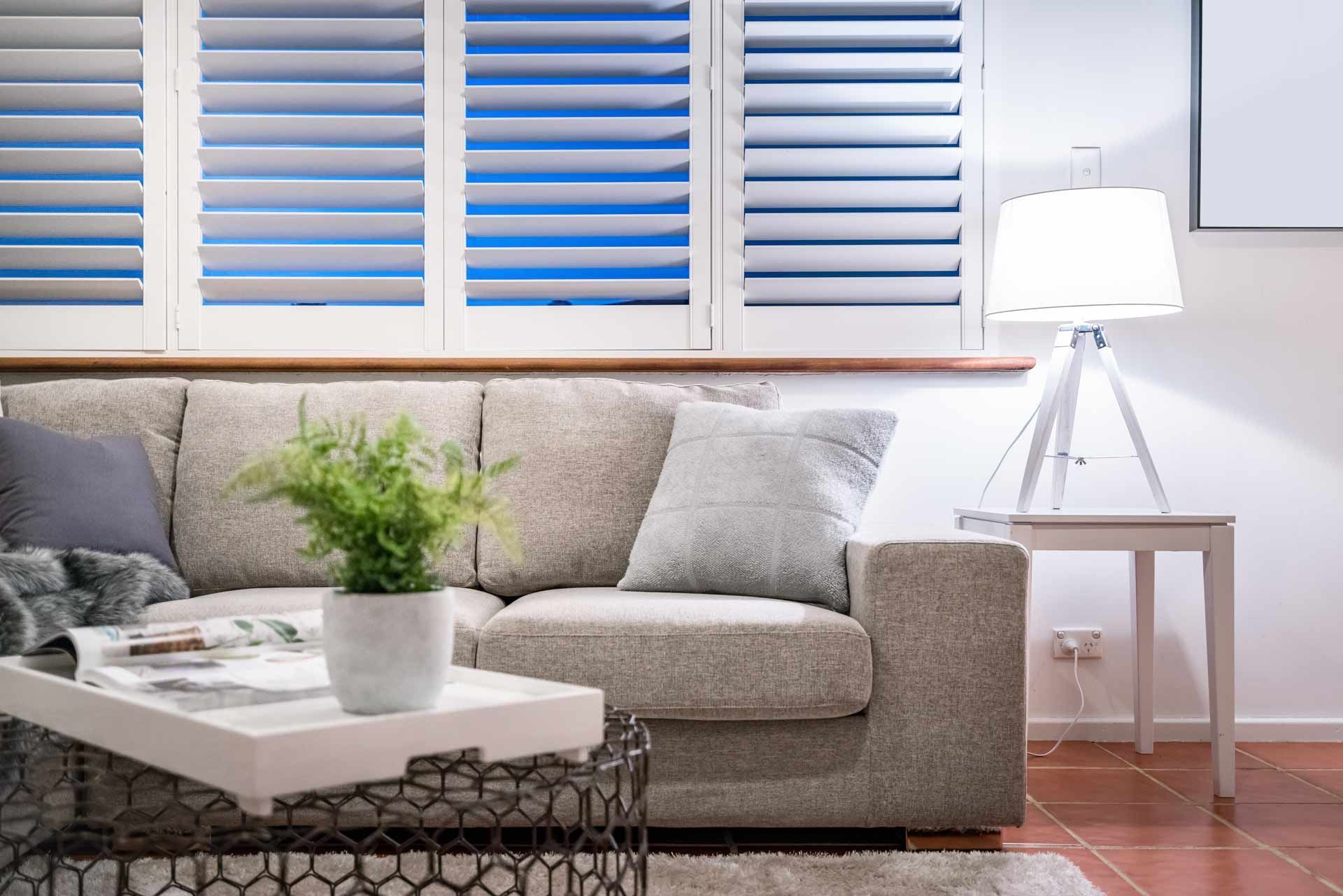 A living room with a couch , coffee table , lamp and shutters.