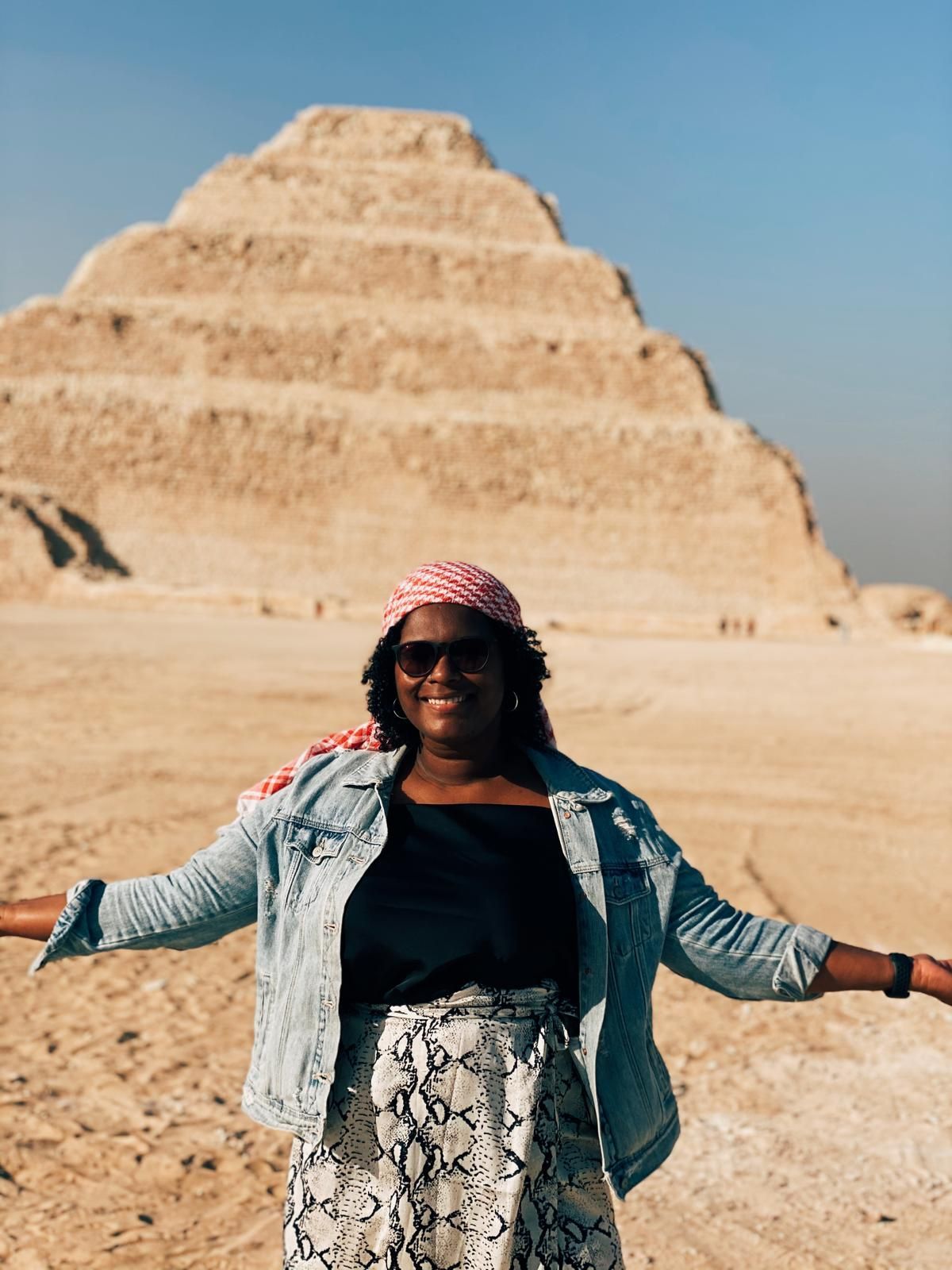 A woman is standing in front of a pyramid in the desert.