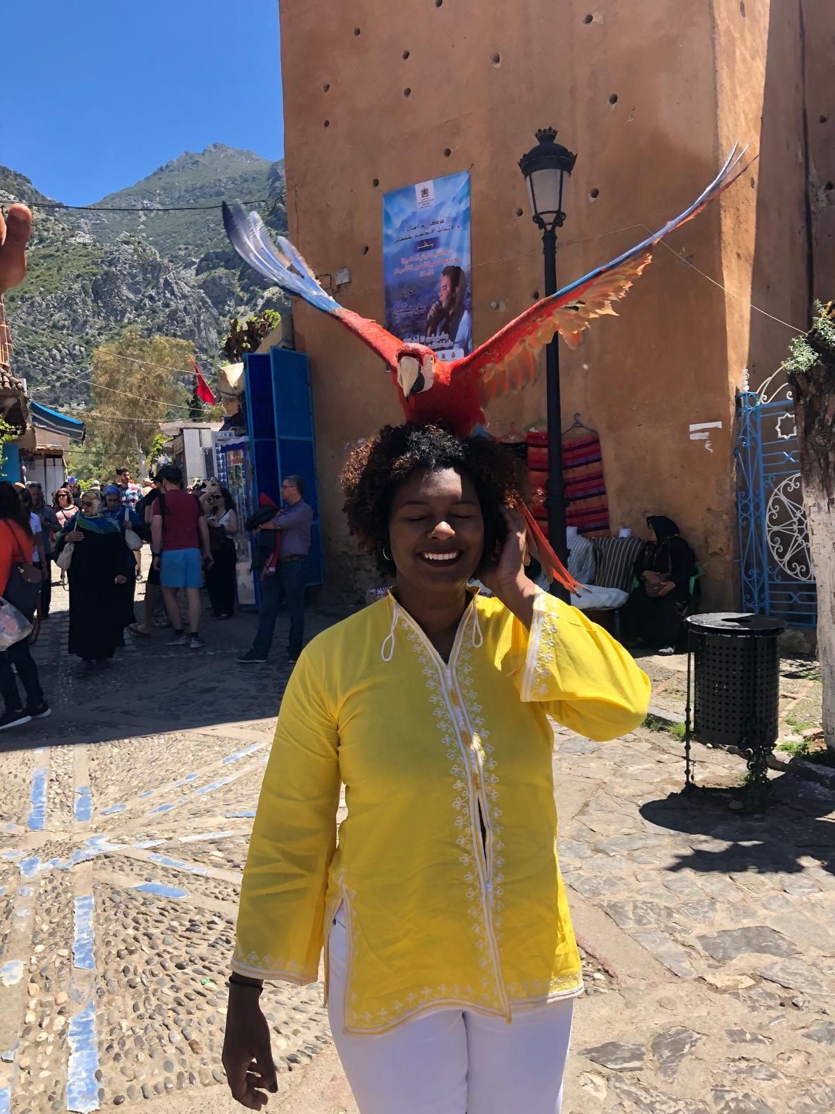 A woman in a yellow shirt is holding a parrot on her head.