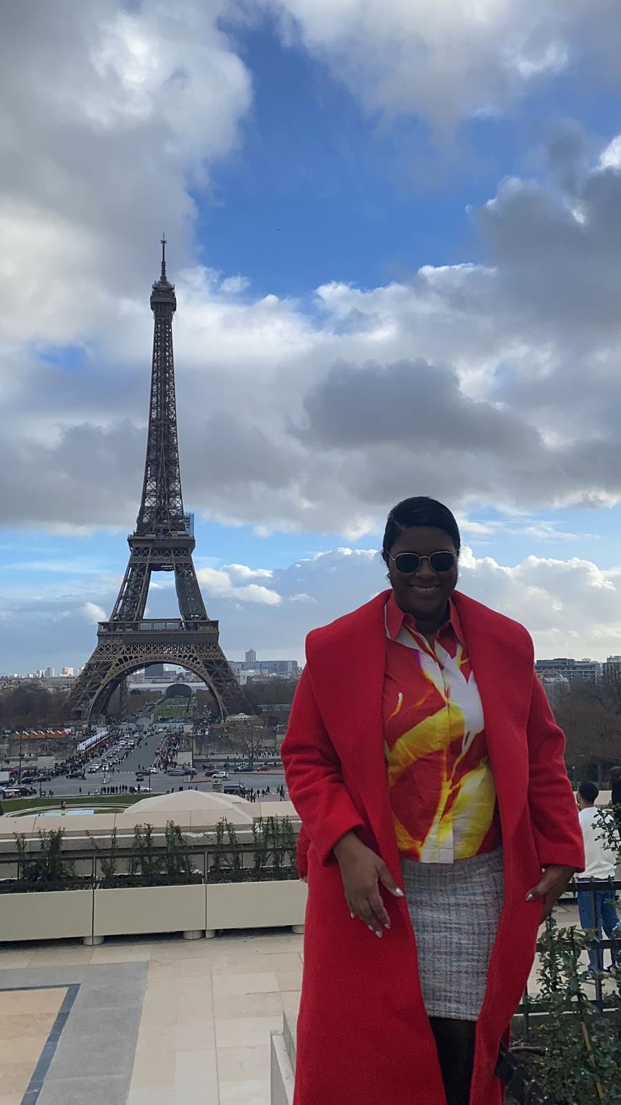 A woman in a red coat is standing in front of the eiffel tower.