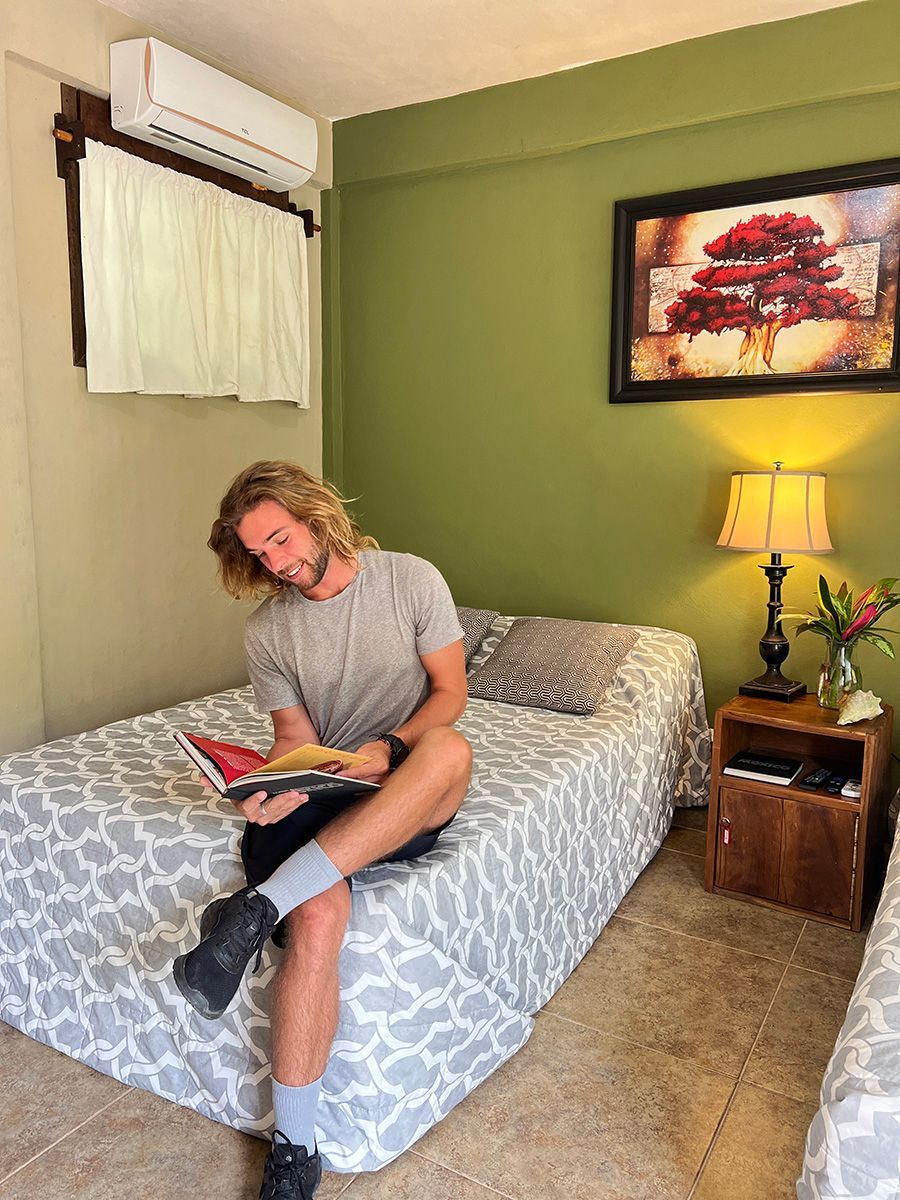 A man is sitting on a bed reading a book.