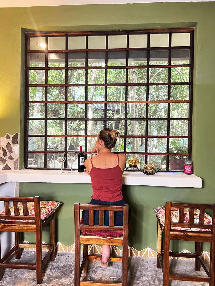 A woman is sitting in a chair in front of a window looking out.