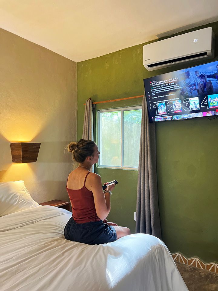 A woman is sitting on a bed watching a television.