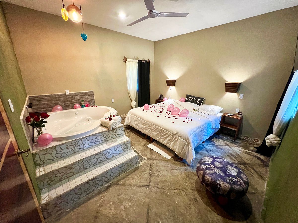 A hotel suite with a bed , jacuzzi tub , stairs and a ceiling fan.