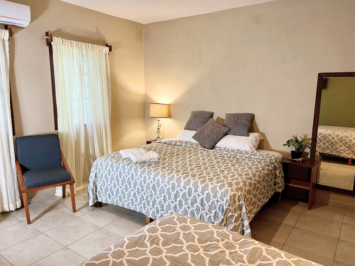 A hotel room with a bed , chair , mirror and air conditioner.