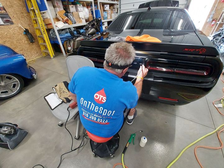 A man in a blue shirt is working on a car in a garage.