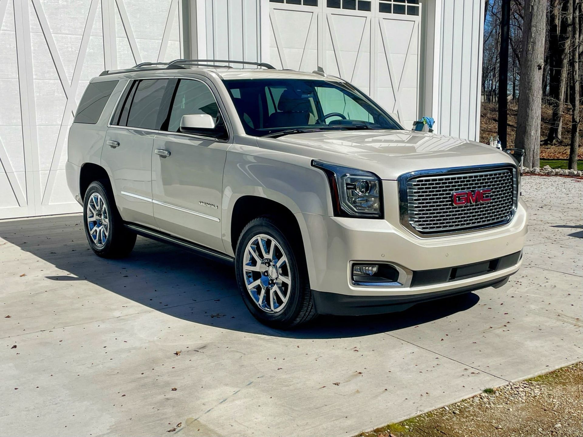 A silver gmc yukon is parked in front of a white garage.