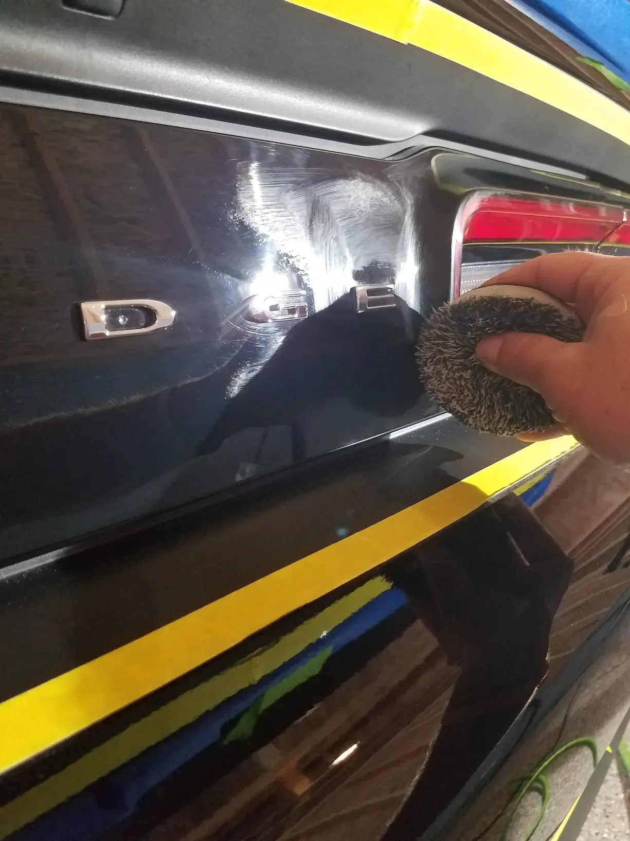 A person is polishing a black car with a sponge