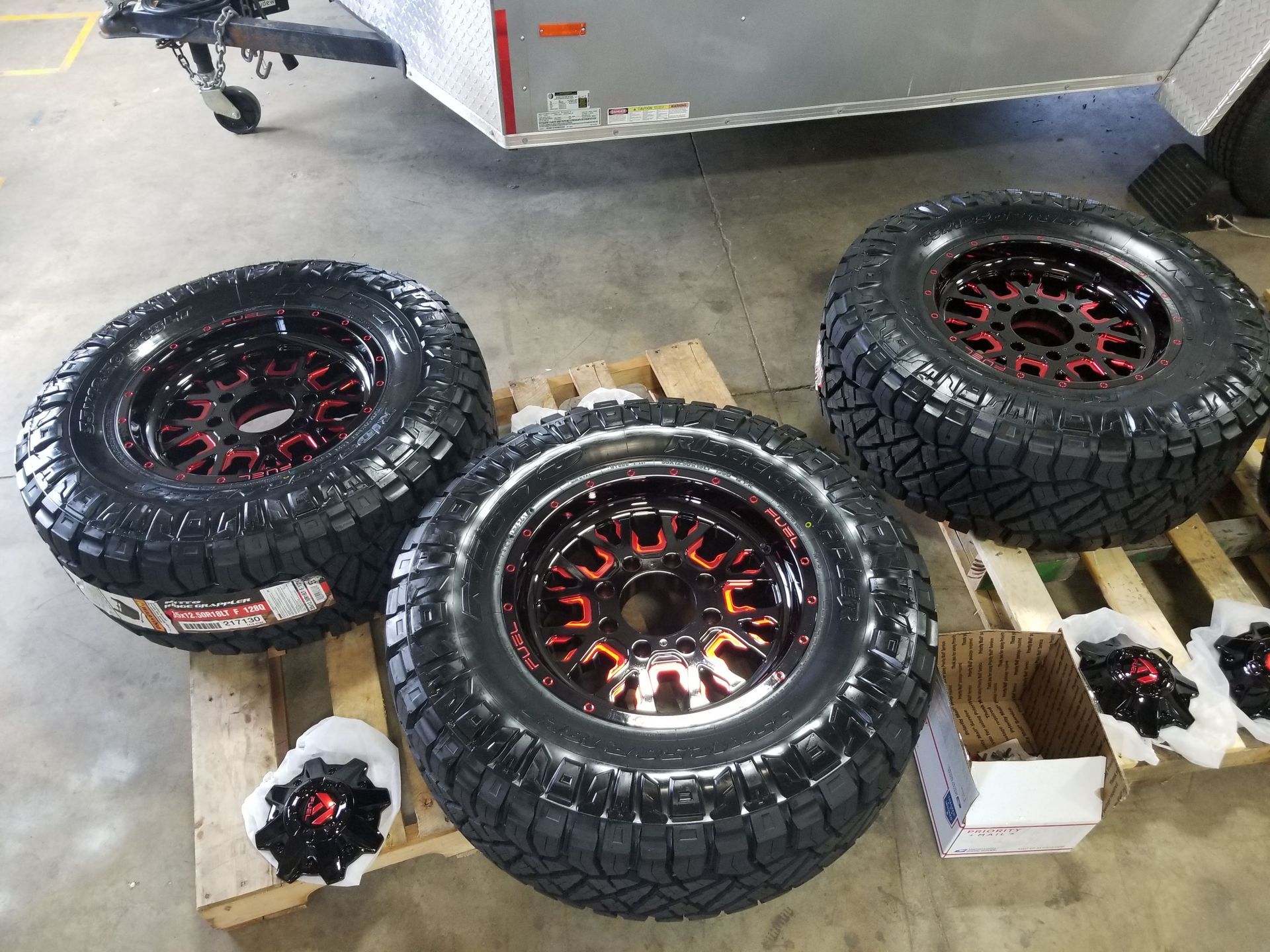 A set of tires and wheels are sitting on a wooden pallet.