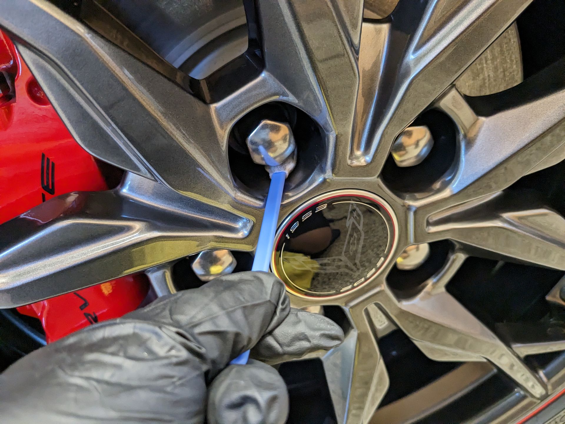 A person is holding a toothbrush in front of a car wheel.