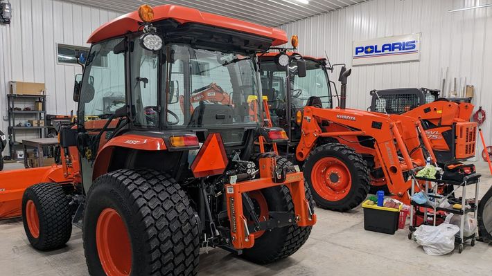 Two orange tractors are parked in a garage.