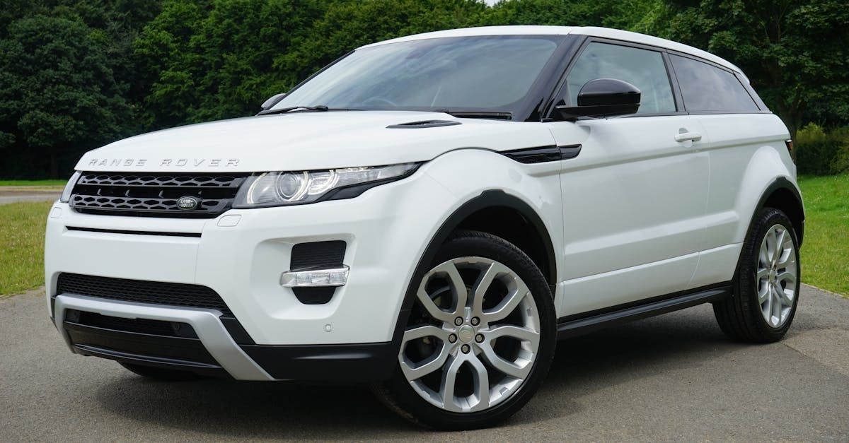 A white Range Rover Evoque SUV parked on asphalt with a green, leafy background.