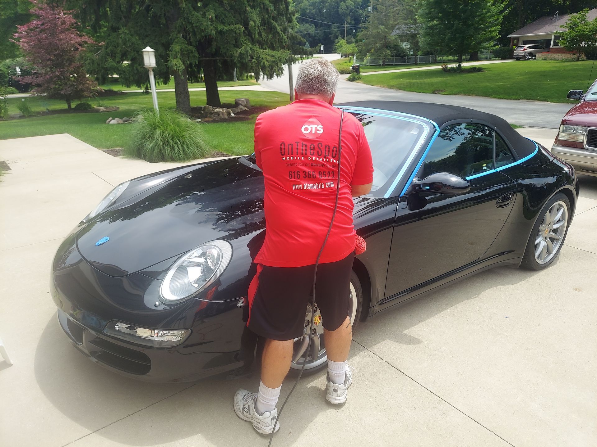A man in a red shirt is standing next to a black car