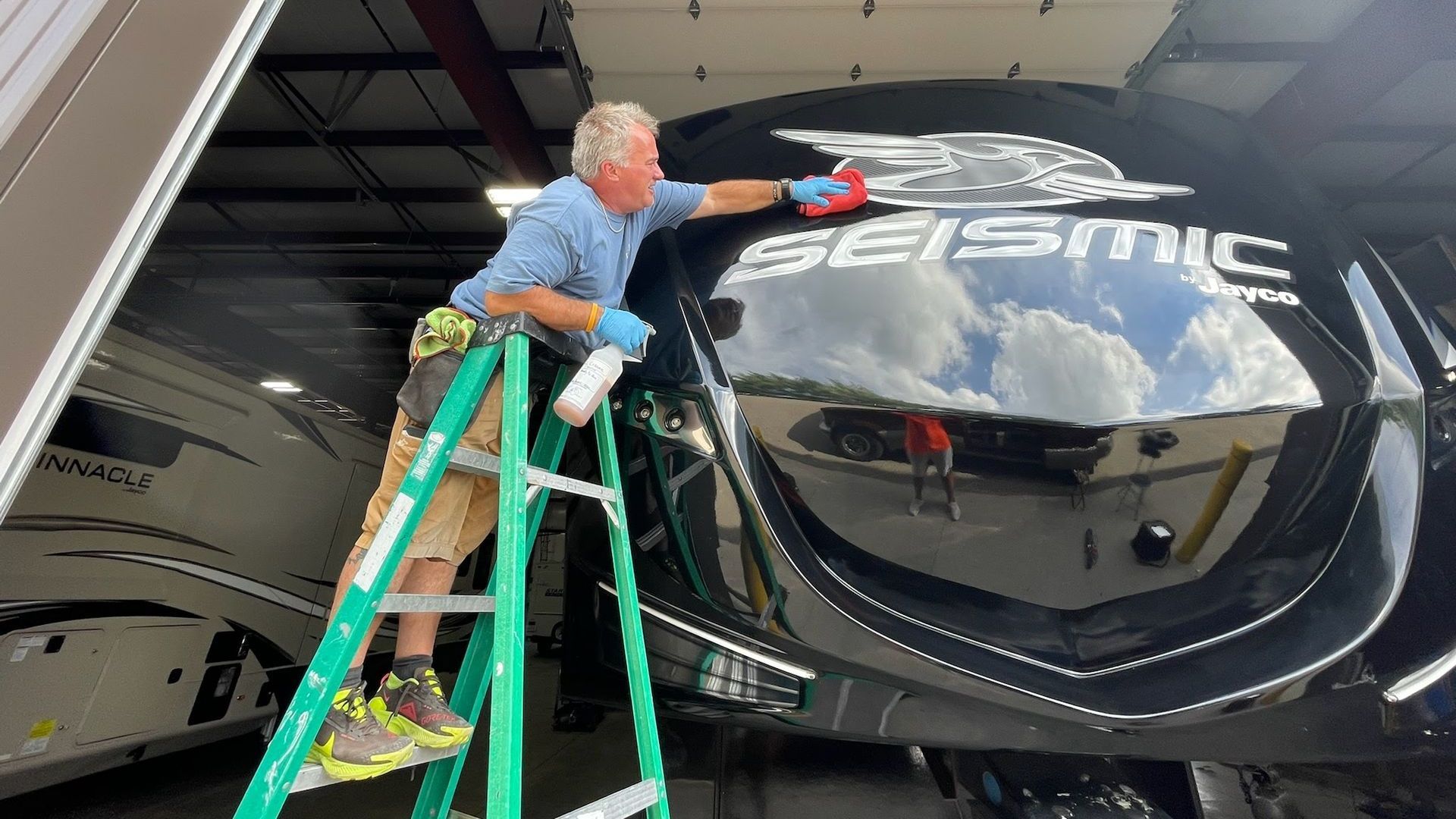 A man is standing on a ladder cleaning the windshield of a rv.