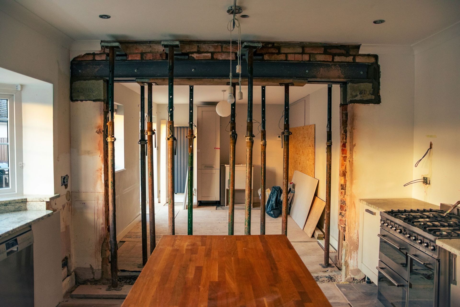 Interior view of a home renovation featuring an exposed steel support beam held up by several vertical temporary props.