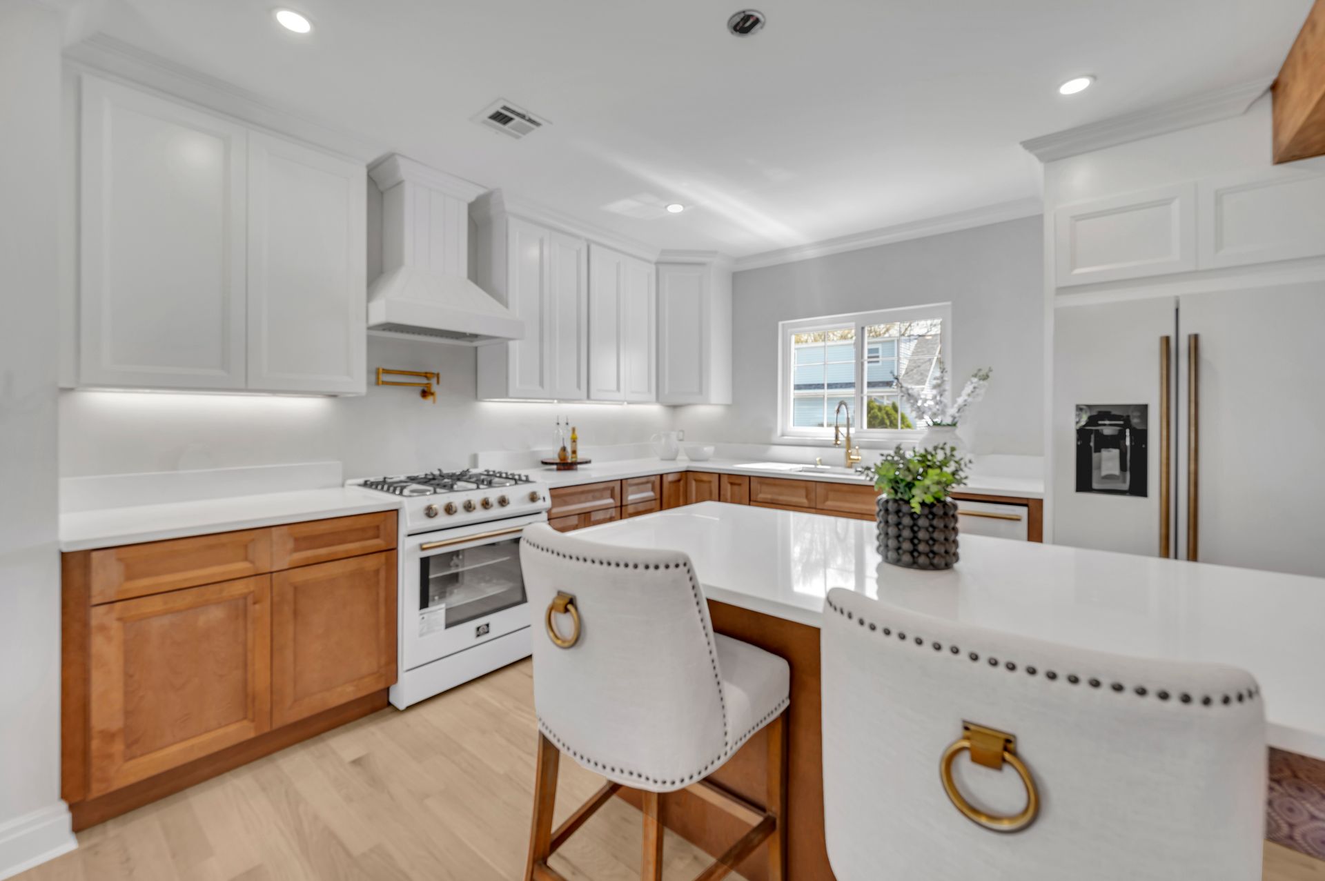 A modern kitchen featuring white upper cabinets, wood-toned base cabinets, a white island, and two upholstered chairs.