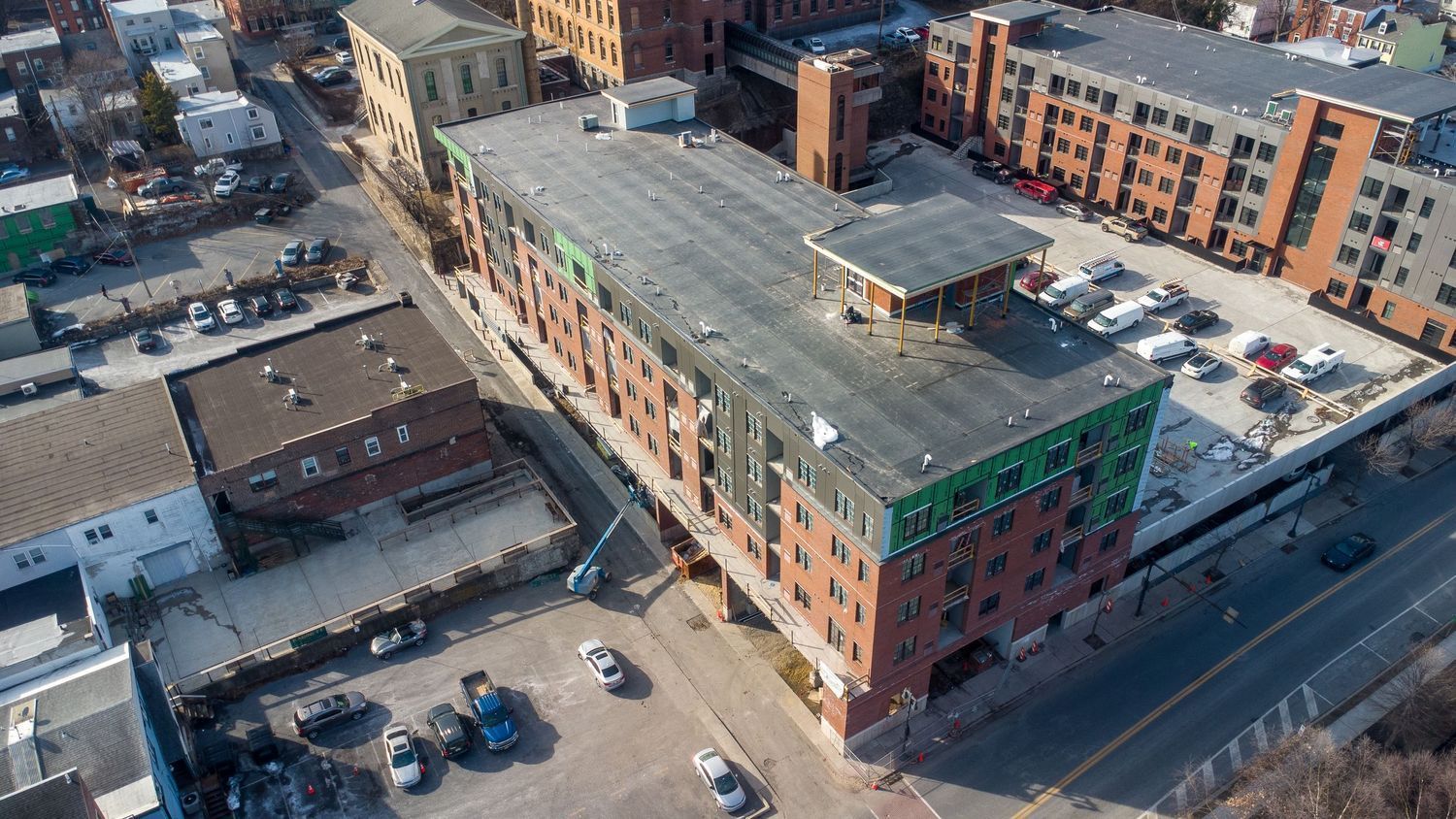 Aerial view of a partially constructed multi-story brick building, surrounding parking lots, and urban street infrastructure.