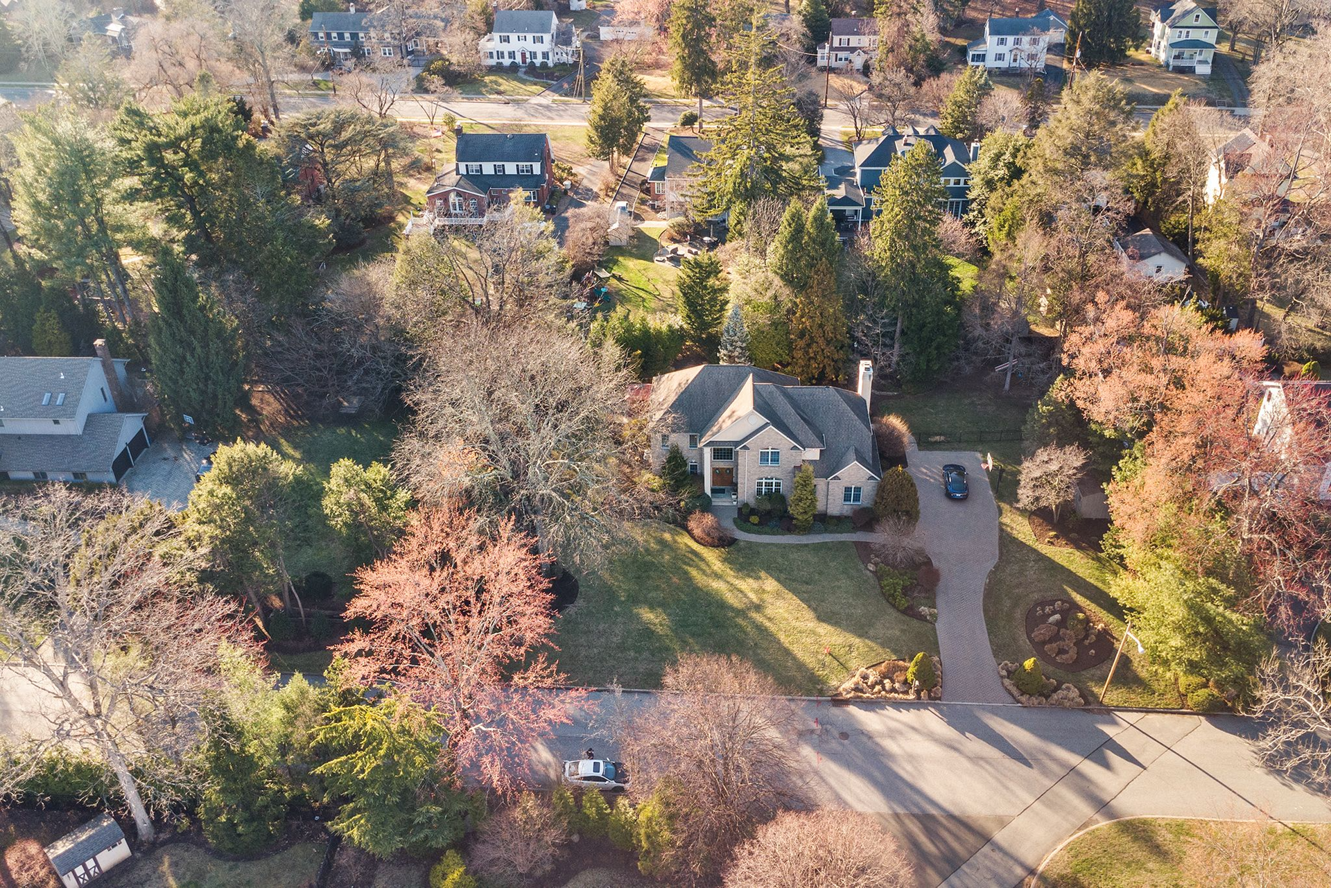 Aerial view of a tan suburban house nestled among dense, multi-colored autumn trees with a curved driveway.